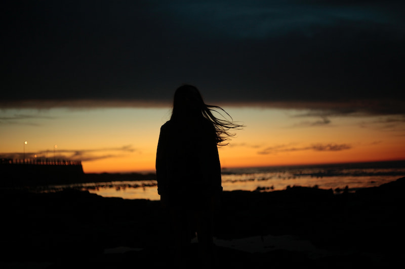 Image of a woman alone watching the sunrise over the sea learning how to deal with loneliness
